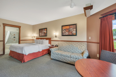 Large bed with white linens and red blanket near white couch and table at The Inn at Ohio Northern University in Ada, OH