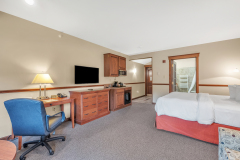 Large bed with white linens and red blanket near white couch in front of desk and entertainment stand at The Inn at Ohio Northern University in Ada, OH