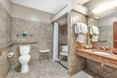 Granite shower with shower seats in shower and outside of shower with white shower curtain near sink and white towels at The Inn at Ohio Northern University in Ada, OH
