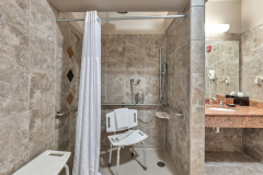 Granite shower with shower seats in shower and outside of shower with white shower curtain near sink and white towels at The Inn at Ohio Northern University in Ada, OH
