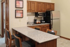 Granite counter top with bar stools near refridgerator and microwave with coffeemaker and wooden cabinets at The Inn at Ohio Northern University in Ada, OH