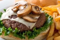 Burger on bun with lettuce, cheese and mushrooms next to french fries on white plate at The Inn at Ohio Northern University in Ada, OH