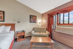 Large bed with white linens and red blanket near coffee table in front of white couch and large air conditioner at The Inn at Ohio Northern University in Ada, OH