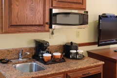 Microwave under wooden cabinets with sink and coffee maker on a shelf next to television at The Inn at Ohio Northern University in Ada, OH