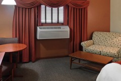 White sofa in front of coffee table next to air conditioner and red curtains near wooden desk at The Inn at Ohio Northern University in Ada, OH