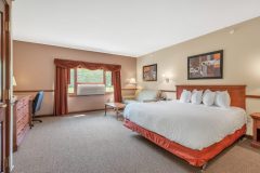 Large bed with white linens and red blanket near coffee table in front of white couch and large air conditioner near stone fireplace at The Inn at Ohio Northern University in Ada, OH
