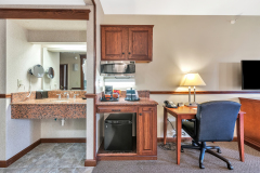 Microwave under wooden cabinets with sink and coffee maker on a shelf next to television at The Inn at Ohio Northern University in Ada, OH