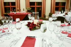 Table with white table cloth with glassware and silverware on top with red napkins and centerpiece with candle and plant near other tables at The Inn at Ohio Northern University in Ada, OH