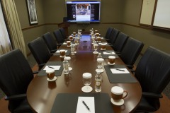 Large wooden table with mugs and water bottles on top with black leather chairs surrounding table in front of large screen displaying website at The Inn at Ohio Northern University in Ada, OH