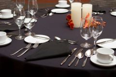 Assorted silverware near glassware and plates on table with black tablecloth near center candle at The Inn at Ohio Northern University in Ada, OH