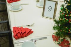 White table and tablecloth next to small christmas tree on top of table with red napkin next to silverware and mugs on plates with framed picture of the number 9 at The Inn at Ohio Northern University in Ada, OH