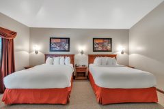 Two queen beds with white linens and red pillows and red blanket with side table in between them at The Inn at Ohio Northern University in Ada, OH