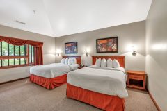 Two queen beds with white linens and red pillows and red blanket near side table at The Inn at Ohio Northern University in Ada, OH