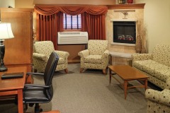 Group of white armchairs near air conditioner near wooden coffee table in front of wooden dresser and wooden desk with black leather chair at The Inn at Ohio Northern University in Ada, OH