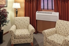 Group of white armchairs near air conditioner near wooden coffee table in front of wooden dresser at The Inn at Ohio Northern University in Ada, OH