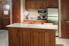 Granite counter top with bar stools near refrigerator and microwave with coffeemaker and wooden cabinets at The Inn at Ohio Northern University in Ada, OH