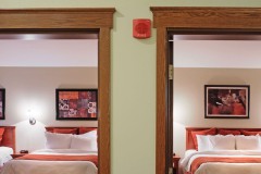 Two open doorways looking into rooms with large beds with white linens and red pillows with red blankets and art hanging on the walls at The Inn at Ohio Northern University in Ada, OH