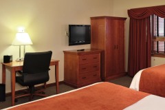 Two large beds with white linens and red blanket in front of TV and dresser next to desk with black leather chair and shelves at The Inn at Ohio Northern University in Ada, OH