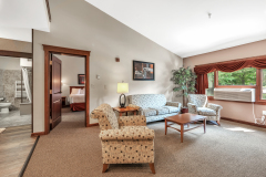 Group of chairs and sofas arranged in circle near side table and lamps in front of red curtains and next to bedroom entrance at The Inn at Ohio Northern University in Ada, OH