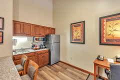 Granite countertop with bar stools near refrigerator and microwave with coffeemaker and wooden cabinets at The Inn at Ohio Northern University in Ada, OH