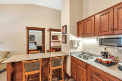 Granite countertop with bar stools near refrigerator and microwave with coffeemaker and wooden cabinets at The Inn at Ohio Northern University in Ada, OH