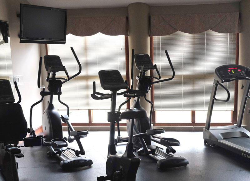 Fitness equipment including treadmill and stairmaster in front of tv neir beige curtains at The Inn at Ohio Northern University in Ada, OH
