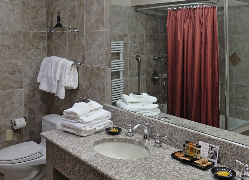 Granite bathroom fixtures with soaps and towels on top of sink in front of red shower curtain at The Inn at Ohio Northern University in Ada, OH