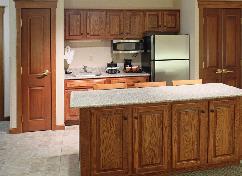Granite counter top with bar stools near refrigerator and microwave with coffeemaker and wooden cabinets at The Inn at Ohio Northern University in Ada, OH
