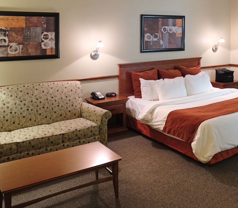 Large bed with white linens and red blanket near coffee table in front of white couch at The Inn at Ohio Northern University in Ada, OH