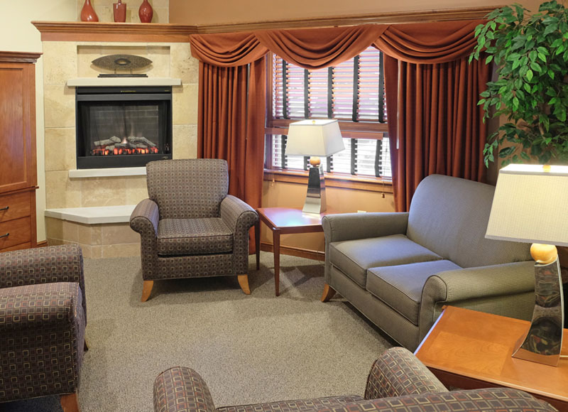 Group of chairs and sofas arranged in circle near side table and lamps in front of red curtains and stone fireplace at The Inn at Ohio Northern University in Ada, OH