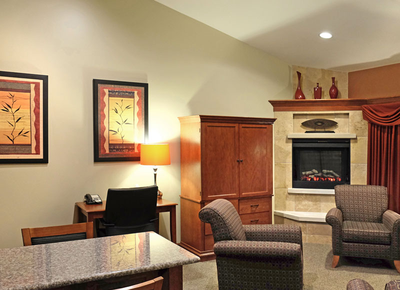 Living room with armchairs near granite table and wooden dresser next to desk and stone fireplace at The Inn at Ohio Northern University in Ada, OH