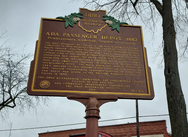 Large sign depicting history of Ada Passenger Depot near large tree in front of stone building near The Inn at Ohio Northern University in Ada, OH