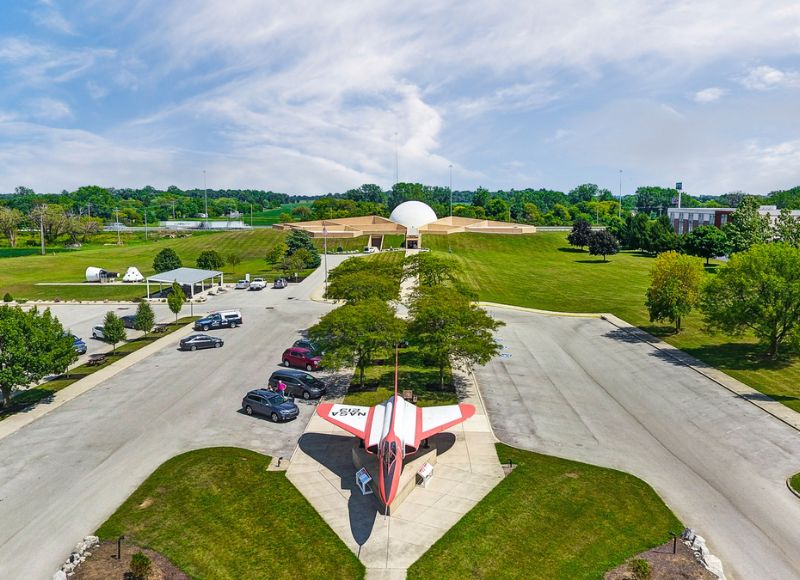 Large parking lot in middle of large green field with airplane museum displays and cars in parking lot leading to large building in distance near trees near The Inn at Ohio Northern University in Ada, OH