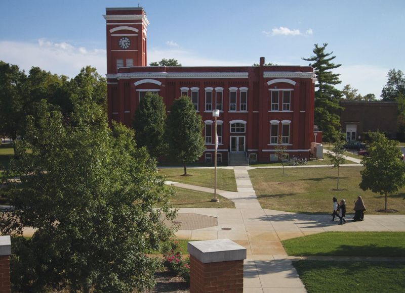 Campus with stone pathways near large green tree on outside of tall brick building with people walking on stone pathway at The Inn at Ohio Northern University in Ada, OH