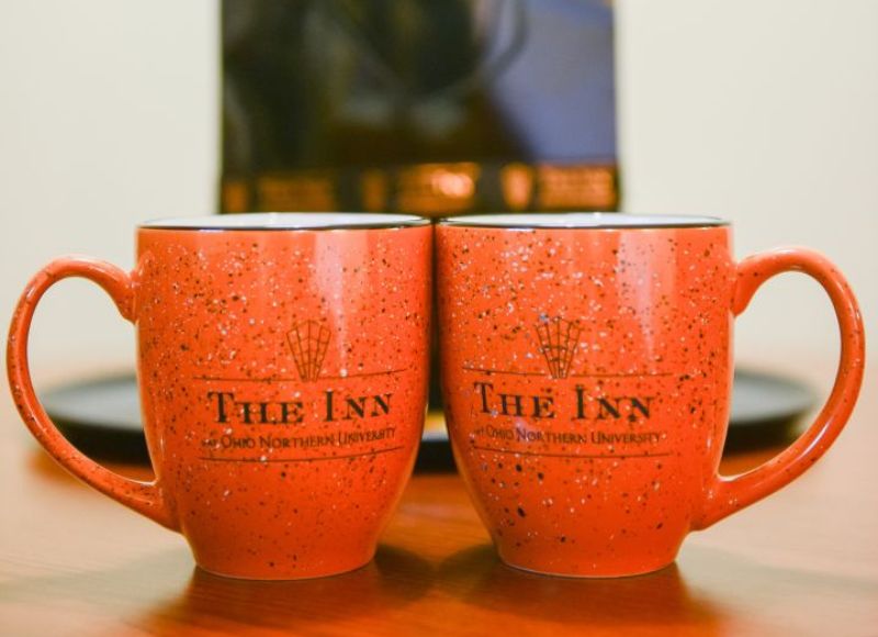 Two red speckled mugs on wooden table in front of artwork and black plate at The Inn at Ohio Northern University in Ada, OH