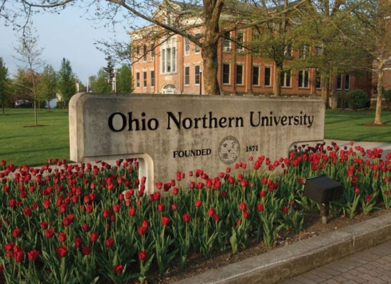 Stone sign for Ohio State University on bed of red flowers in front of trees and stone building at The Inn at Ohio Northern University in Ada, OH