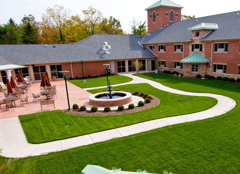 Courtyard with lawn chairs and umbrellas near brick building and stone fountain and pathway at The Inn at Ohio Northern University in Ada, OH