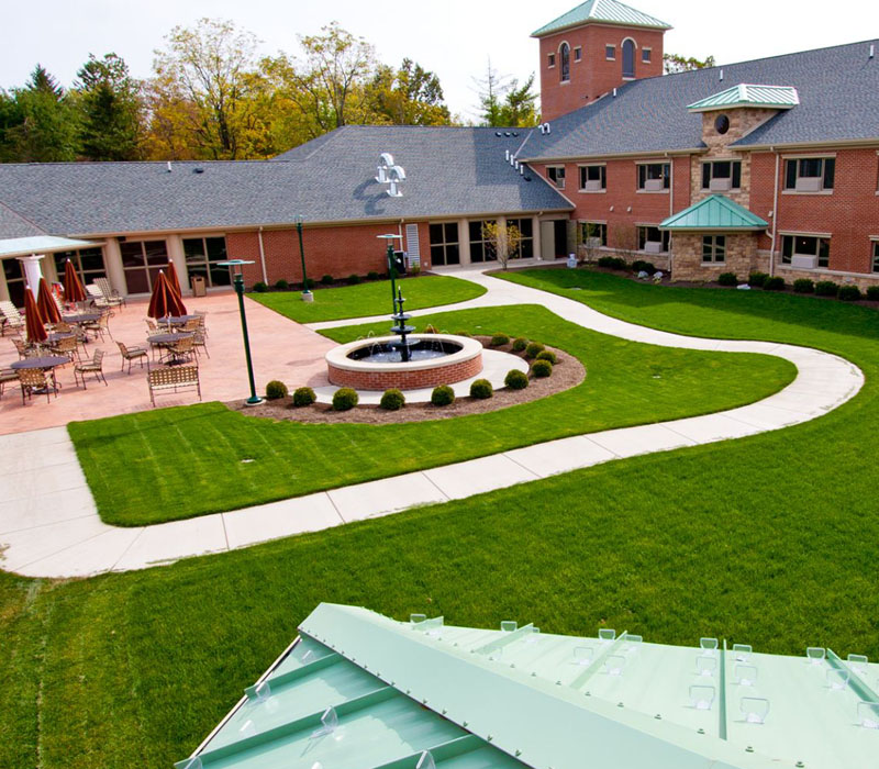 Courtyard with lawn chairs and umbrellas near brick building and stone fountain and pathway at The Inn at Ohio Northern University in Ada, OH