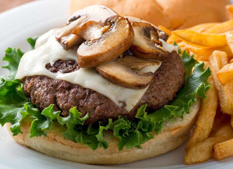 Burger on bun with lettuce, cheese and mushrooms next to french fries on white plate at The Inn at Ohio Northern University in Ada, OH