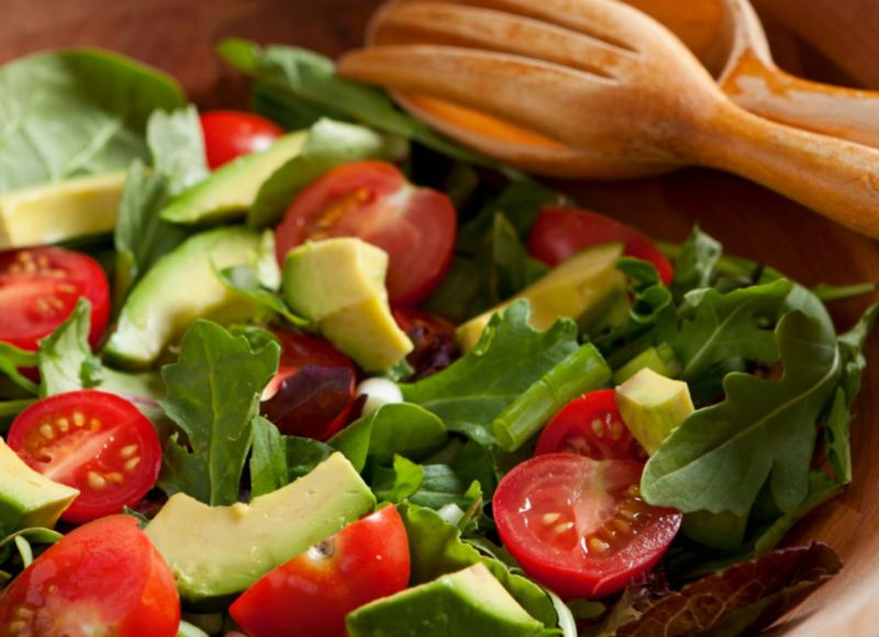 Green salad with lettuce, spinach, tomatoes and avacados in wooden bowl near wooden spoon at The Inn at Ohio Northern University in Ada, OH