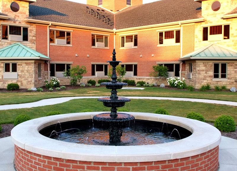 Stone fountain with black centerpiece and water near brick building and foliage at The Inn at Ohio Northern University in Ada, OH