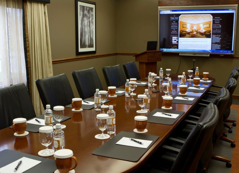 Large wooden table with mugs and water bottles on top with black leather chairs surrounding table in front of large screen displaying website at The Inn at Ohio Northern University in Ada, OH