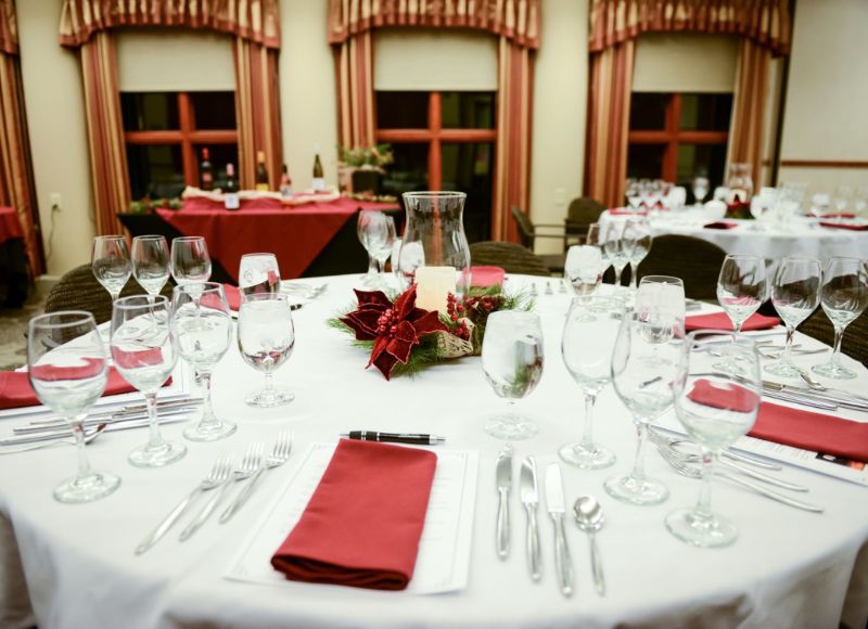 Table with white table cloth with glassware and silverware on top with red napkins and centerpiece with candle and plant near other tables at The Inn at Ohio Northern University in Ada, OH
