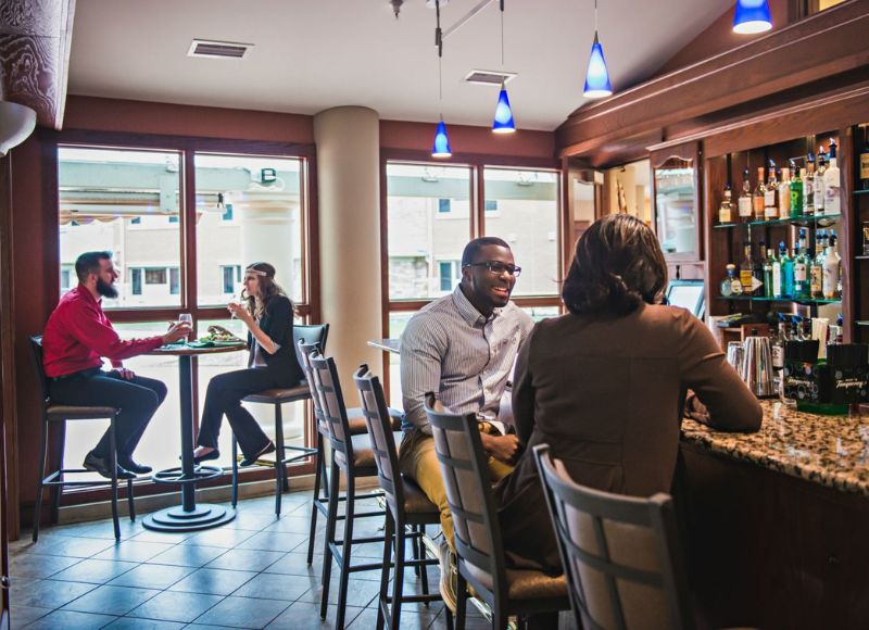 People at bar conversing near two people sitting at table eating in front of bar with assortment of alcohols on shelves at The Inn at Ohio Northern University in Ada, OH